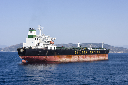 Greece, near Piraeus: Big tanker Golden Energy on blue ocean water with skyline of mountain chain in the background - concept transport boat ship sea travel oil business energy supply. April 28, 2018のeditorial素材