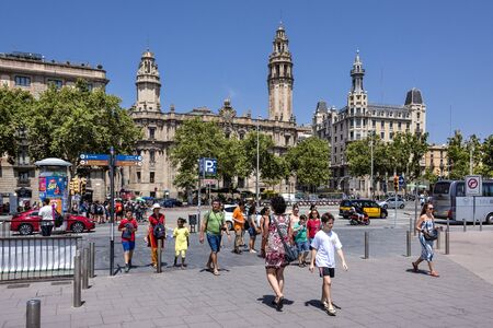 Spain, Barcelona, near harbor: Daily street scene at Passeig de Colom crossing in the city center of the Spanish town with old post office, people, tourists, men, women and blue sky. July 01, 2018のeditorial素材