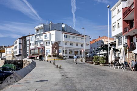 Spain, Finisterre: City center with harbor, colorful boats, houses, restaurants, cars, blue sky. The town is located on a rock-bound peninsula and was famous for being end of the world. July 12, 2018のeditorial素材