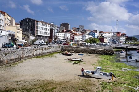 Spain, Finisterre: Panoramic view of Spanish city center with harbor at low tide, colorful boats, skyline, cityscape and blue sky. The region was famous for being the end of the world. July 12, 2018のeditorial素材