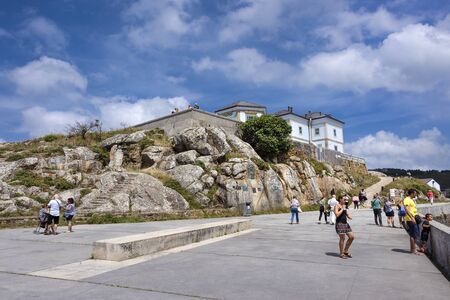 Spain, Finisterre: People tourists pilgrims visit famous lighthouse with rocky cliff, skyline and blue sky in the background. The building is located on a rock-bound peninsula. July 12, 2018のeditorial素材