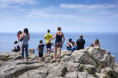 Spain, Finisterre: People tourists pilgrims on rocky cliff, ocean water, skyline and blue sky Scene takes place on rock-bound peninsula which was famous for being the end of the world. July 12, 2018のeditorial素材