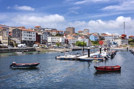 Spain, Finisterre: Panoramic view of Spanish city center with harbor at high tide, colorful boats, skyline, cityscape and blue sky. The region was famous for being the end of the world. July 12, 2018のeditorial素材