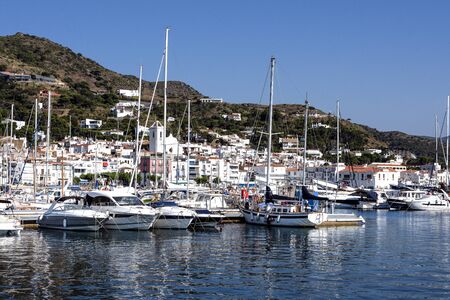 Spain, Catalonia, El Port de la Selva:  White yachts in the marina of the Spanish town with mediterranean sea, white houses, green hill and blue sky in the background - concept travel. June 27, 2018のeditorial素材