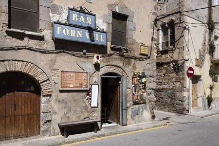 Spain, Catalonia, Castello d'Empuries: Exterior wall of old town bar with entrance door, pub sign, house facade and street in the city center of the famous old medieval Spanish town. June 29, 2018のeditorial素材