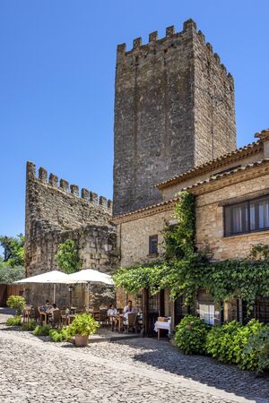 Spain, Catalonia, Peratallada: People tourists residents in a restaurant under famous Castle of Peratallada in the center of the small fortified medieval Spanish town with blue sky. June 30, 2018のeditorial素材