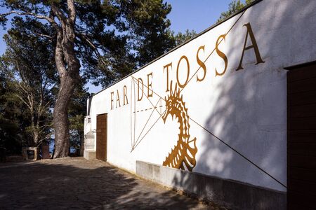 Spain, Catalonia, Costa Brava, Tossa de Mar: Side view of famous lighouse building in dramatic afternoon light with green trees and blue sky in the background - concept travel nautical. June 30, 2018のeditorial素材