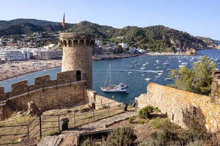 Spain, Catalonia, Costa Brava, Tossa de Mar: Panoramic view over famous old town, mediterranean sea, bay, long beach, cityscape, hill chain and blue sky in the background - travel. June 30, 2018のeditorial素材