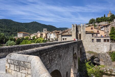 Spain, Catalonia, Besalu: Panorama view on the famous skyline of old ancient fortified Spanish town with bridge, river EL Fluvia, tower, green trees and blue sky in the background. June 27, 2018のeditorial素材