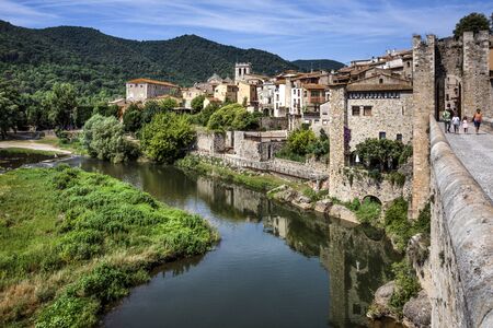 Spain, Catalonia, Besalu: Panorama view on the famous skyline of old ancient fortified Spanish town with bridge, river EL Fluvia, tower, green trees and blue sky in the background. June 27, 2018のeditorial素材