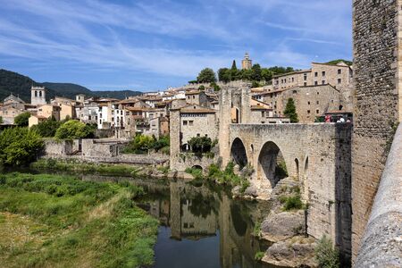 Spain, Catalonia, Besalu: Panorama view on the famous skyline of old ancient fortified Spanish town with bridge, river EL Fluvia, tower, green trees and blue sky in the background. June 27, 2018のeditorial素材
