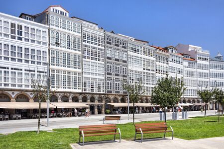 Spain, Galicia, La Coruna, A Corunna: Row of apartment building houses with traditional white wooden balconies facades in the city center of Spanish town with public park and blue sky. July 13, 2018のeditorial素材