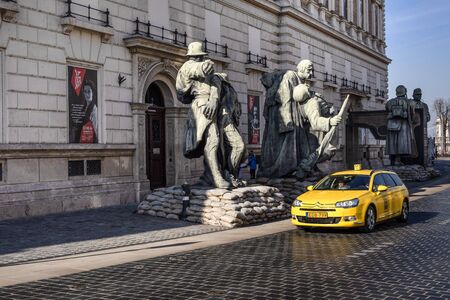 Hungary, Budapest, Miklos: Street scene with yellow Citroen taxi on cobblestone next to big soldier statues in the city center of the Hungarian capital - concept public transport. Feb 06, 2019のeditorial素材