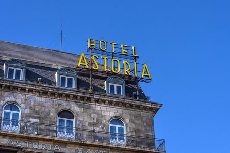 Hungary, Budapest: Big yellow Hotel Astoria neon sign on a roof top in the city center of the Hungarian capital with blue sky in the background - concept advertisment holdiday travel. Feb 06, 2019のeditorial素材