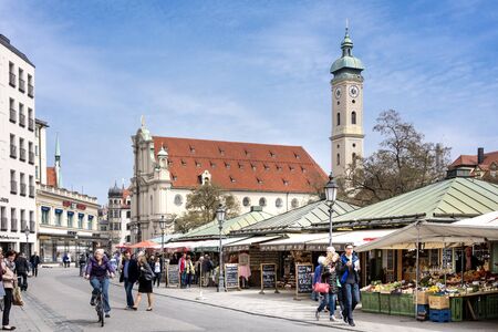 Germany, Bavaria, Munich, Viktualienmarkt: Daily scene with people tourists citizens on the streets of the Bavarian capital with Holy Ghost Church and blue sky in the background. April 22, 2016のeditorial素材