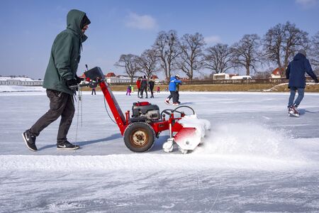Germany, Bavaria, Munich, Nymphenburg Palace: Man with red snow pusher prepares icy frozen lake for ice skating in a public German park. February 28, 2018のeditorial素材