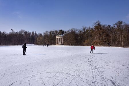 Germany, Bavaria, Munich, Nymphenburg Palace: Winter snow scene with ice skating people and famous Temple of Apollo at Badenburger See in the castle garden of the Bavarian capital. February 28, 2018のeditorial素材