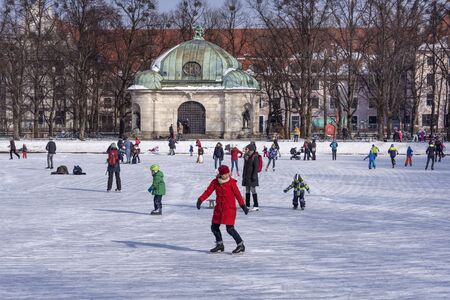 ermany, Bavaria, Munich, Hubertusbrunnen: Happy colorful dressed people men women children while ice skating on white frozen lake water at winter time - concept winter activities. February 28, 2018のeditorial素材