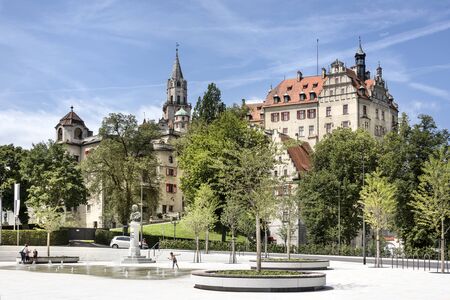 Germany, Sigmaringen, upper Danube: Famous ancient Hohenzollern castle overlooks a modern central park in the city center of the German town with water fountain, green trees, blue sky. July 31, 2017のeditorial素材