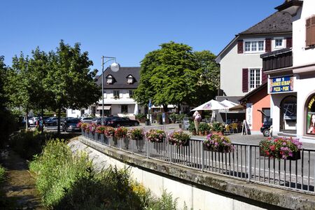 Germany, Heitersheim: Street scene in the center of the German small town with restaurants, shops, buildings, houses, calm river, big green trees and deep blue sky in the background. June 23, 2018のeditorial素材