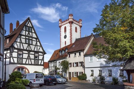 Germany, Hesse, Hanau, Steinheim: White tower of parish church St. John the Baptist in the city center of the German town with street, cars, half-timbered houses and blue sky. September 11, 2018のeditorial素材