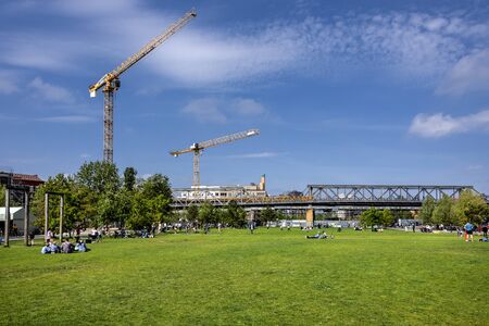 Germany, Berlin, Kreuzberg, Park am Gleisdreieck: Panorama view green lawn, people, trees, yellow cranes, metro subway viaduct and blue sky in the city center of the German capital. May 01, 2019のeditorial素材