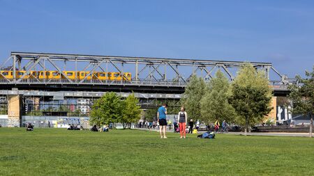 Germany, Berlin, Kreuzberg, Park am Gleisdreieck: Panorama view green lawn, young people, trees, yellow metro subway, metal viaduct and blue sky in the city center of the German capital. May 01, 2019のeditorial素材