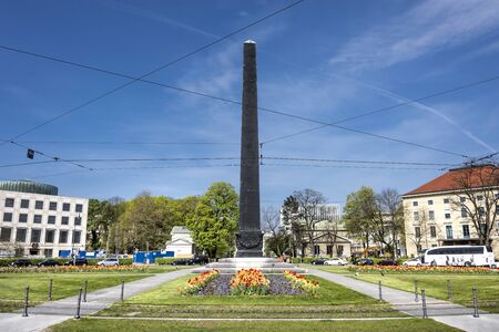 Germany, Bavaria, Munich, Karolinenplatz: Roundabout, obelisk, flowers and buildings in the city center of the Bavarian capital with blue sky in the background. April 22, 2016のeditorial素材