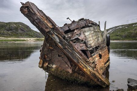 Russia, Arctic, Kola Peninsula, Barents Sea, Teriberka: Front view of abandoned fishing boat shipwreck at low tide near historical fishing harbor of the old Russian settlement small fishing village.の写真素材