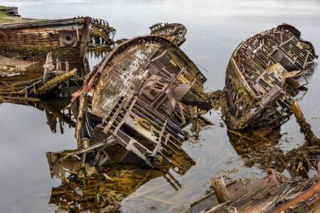 Russia, Arctic, Kola Peninsula, Barents Sea, Teriberka: Rusty abandoned fishing boat shipwrecks at low tide near the historical fishing harbor of the old Russian settlement small fishing village.の写真素材