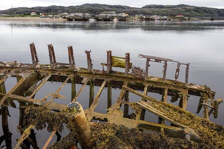 Russia, Arctic, Kola Peninsula, Barents Sea, Teriberka: Rusty abandoned fishing boat shipwreck at low tide near the historical fishing harbor of the old Russian settlement small fishing village.の写真素材