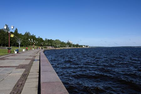 Russia, Karelia, Petrozavodsk: Long riverwalk with calm deep blue water of Lake Onega, people, public park, green trees, lamp posts and blue sky in the city center of the Russian town. Jul 10, 2019のeditorial素材