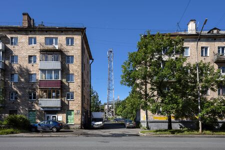 Russia, Karelia, Petrozavodsk: Street scene with typical apartment buildings, parking cars vehicles, green trees, radio mast pole, blue sky near the city center of the Russian town. Jul 10, 2019のeditorial素材