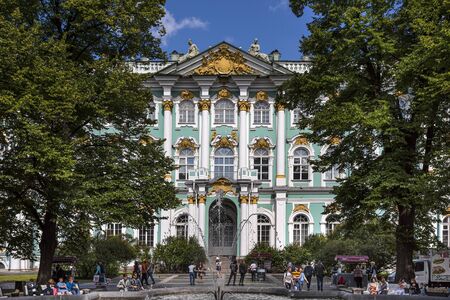 Russia, Saint Petersburg, near Neva river and Palace Garden: Street scene with people tourists next to famous Winter Palace in the city center of the Russian town, green trees, blue sky. Jul 08, 2019のeditorial素材