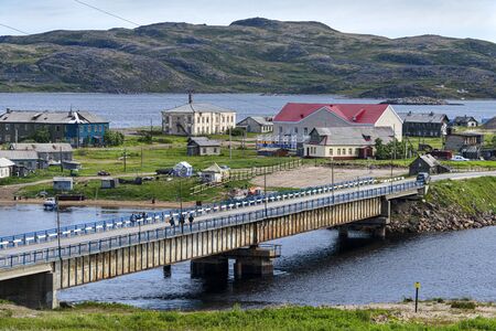 Russia, Arctic, Kola Peninsula, Barents Sea, Teriberka: Road bridge to the oldest part of old Russian settlement small village with fishing boats, old houses, hilly skyline - travel. Jul 19, 2019のeditorial素材