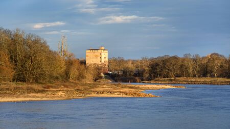 Germany, Saxony-Anhalt, Dessau-Rosslau: Elbe river in late afternoon sun light with abondoned tower, trees, calm floating water and blue sky in background - concept public park nature riverbank.のeditorial素材