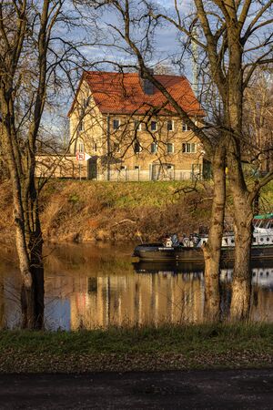 Germany, Saxony-Anhalt, Dessau-Rosslau: Mulde river with house, reflections on calm water, trees and cargo boat near Leopoldshafen and the city center of the famous German town - travel. Dec 30, 2019のeditorial素材
