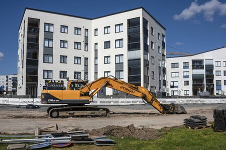 Finland, Rovaniemi: Hydraulic yellow excavator at building site with new white apartment buildings - concept building architecture work economics equipment boom business real estate. Jul 27, 2019のeditorial素材