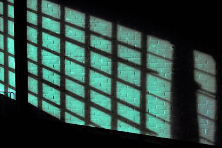 Dark green quadratic shadow on a stonework wall illuminated by golden sunlight - concept dramatic contrast film noir mystic interior texture background surface structure window close up detail eveningの写真素材