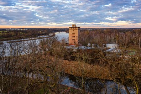 Germany, Saxony-Anhalt, Dessau-Rosslau: Aerial view of Elbe river in late afternoon sun light with abondoned tower, trees, calm floating water and blue sky - concept public park nature riverbank.の写真素材