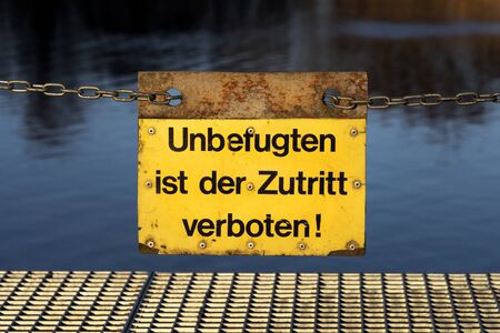 Yellow German sign on a metal chain: No access - no entry for unauthorised persons! (Unbefugten ist der Zutritt verboten!)の写真素材