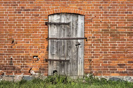 Old wooden door with metal fittings, red brick stone facade and green lawn.の写真素材