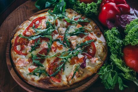 fresh Italian pizza, with tomatoes, caviar and arugula on a thin cake. The pizza rests on a wooden round board around decorated with vegetablesの写真素材
