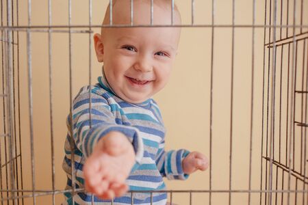 Funny cute kid sits in a cage. He smiles and slips a pen through the window between the bars.の写真素材