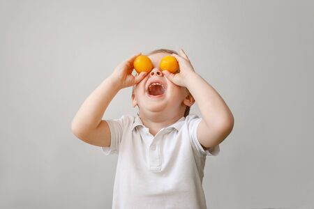 A very funny todler boy indulges with orange fruit, he put the fruit on his eyes and laughs.の写真素材