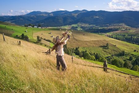 a girl with long hair in a straw hat stands on a hill and admires flowers. A girl stands at sunset...