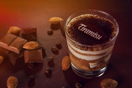 tiramisu dessert in a glass on a brown background. Pieces of shekolada and cocoa beans are laid out aroundの写真素材