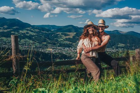 a girl and a man stand high in the mountains, they laugh and hug. The girl has beautiful long hair and a straw hat. A pair of lovers walks on a field high in the mountainsの写真素材