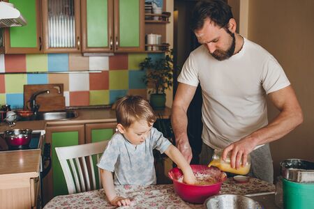 Dad and three-year-old cook at home in the kitchen. The child helps dad cook the cake.の写真素材