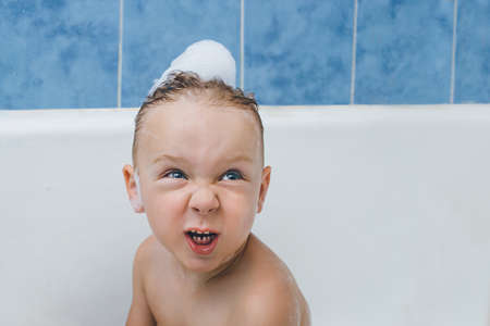 Emotional baby grimaces while washing in the bathroom with foam. about makes a disgruntled wicked grimaceの写真素材